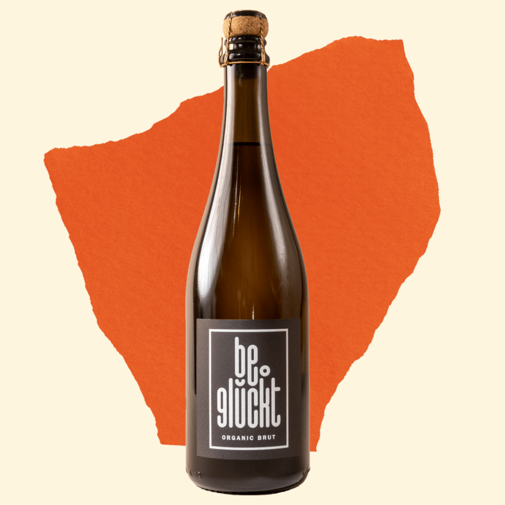 be°glückt Organic Brut Flasche auf orangefarbenem Hintergrund – Hausmarke von be°bubbly