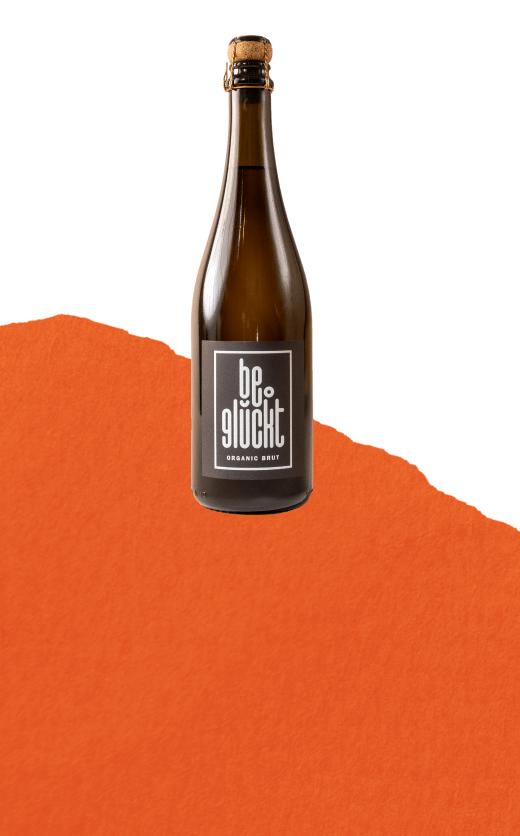 be°glückt Organic Brut Flasche auf orangefarbenem Hintergrund – Hausmarke von be°bubbly